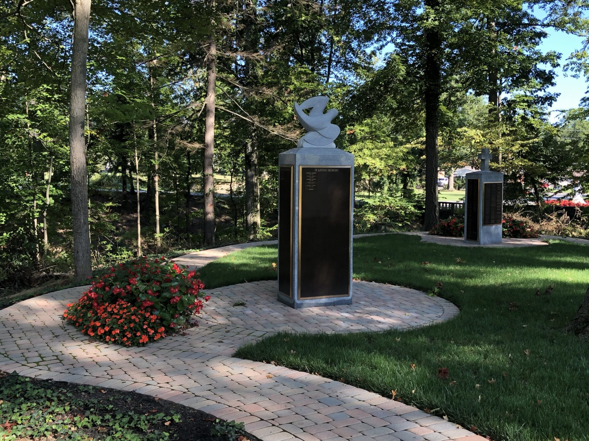 Photo of a statue with a bird on top and red flowers at the Whispering Winds sculptures